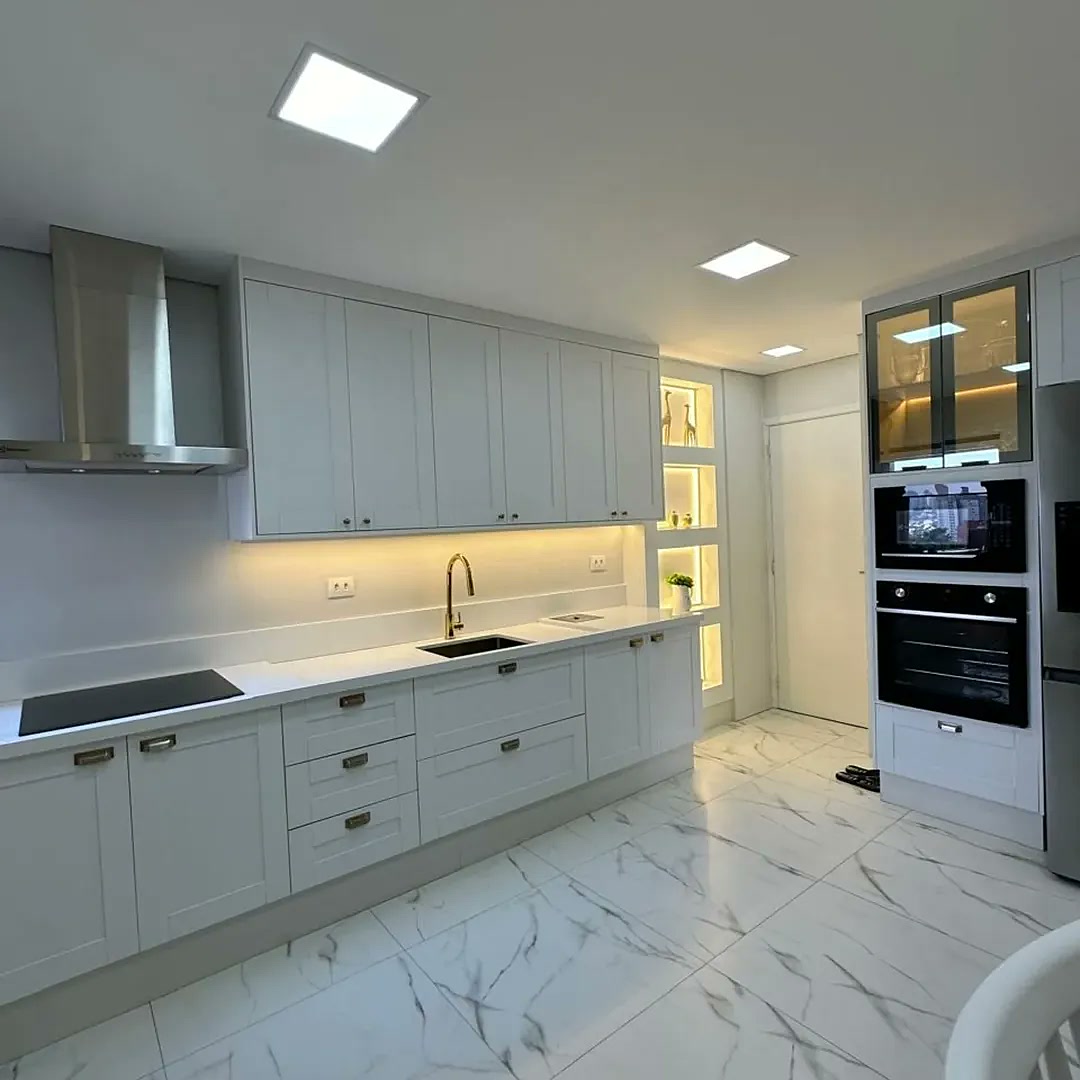 Cozinha planejada branca estilo clássico com torre de forno, coifa inox, nichos LED e piso mármore – projeto real Estillo Design São Paulo
