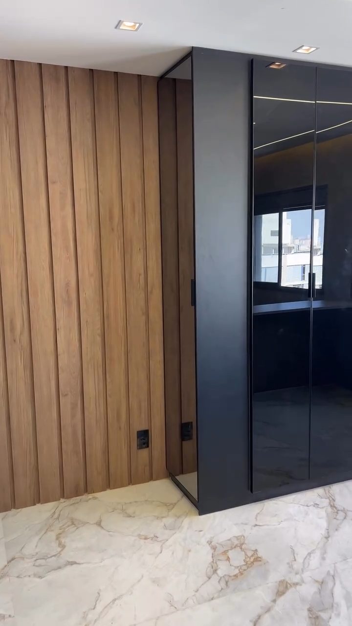 Painel ripado em madeira do piso ao teto ao lado de guarda-roupa preto laqueado com portas de vidro, projeto Estillo Design